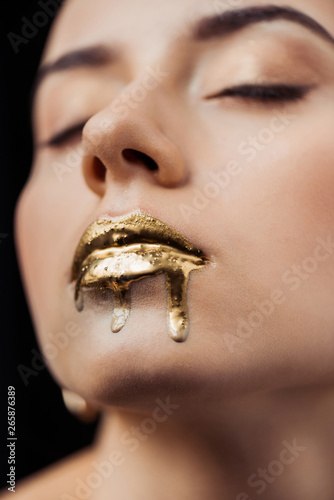 close up of young woman with closed eyes and golden painted lips isolated on black