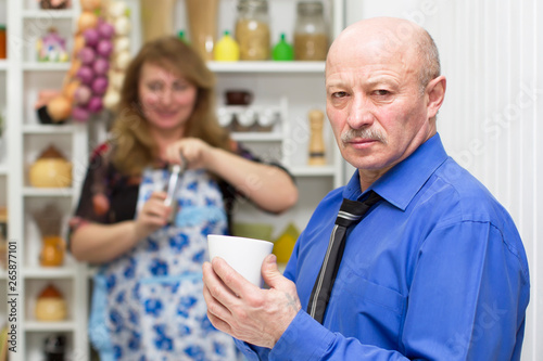 Elderly man with a cup on the background of his wife