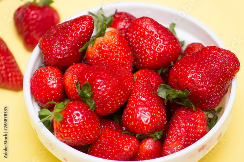 Fresh strawberries in bowl close up on yellow background