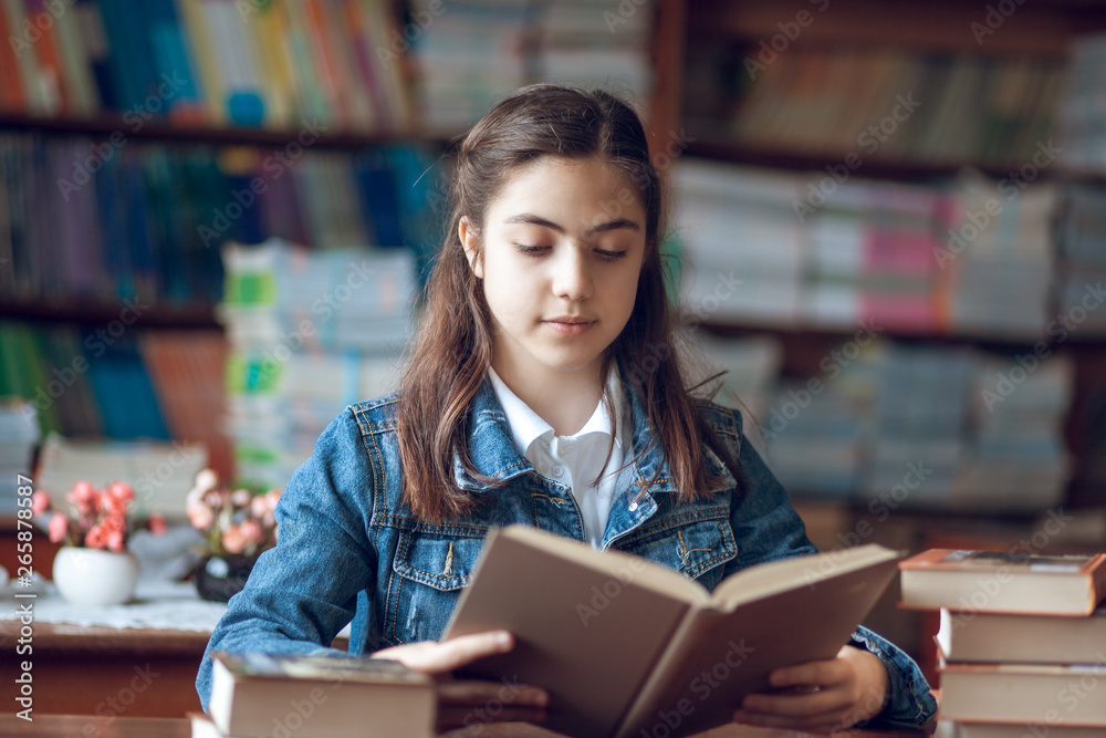 beautiful schoolgirl sitting in the library and reading a book beautiful schoolgirl sitting in the library and reading a book