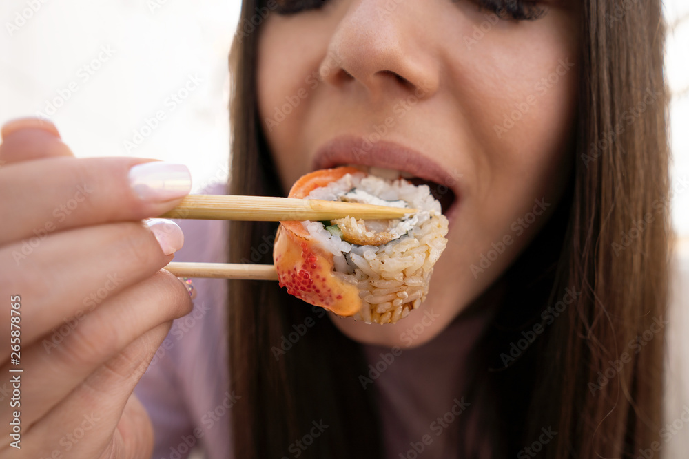 Sushi and mouth girl closeup. The girl eats sushi and rolls with chopsticks Sushi and mouth girl closeup. The girl eats sushi and rolls with chopsticks