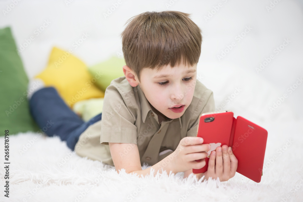Child with a mobile phone. Schoolboy with a smartphone lying on the bed. Kids and Gadgets Child with a mobile phone. Schoolboy with a smartphone lying on the bed. Kids and Gadgets