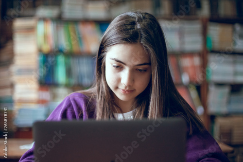 pretty school girl studying in the school library using laptop