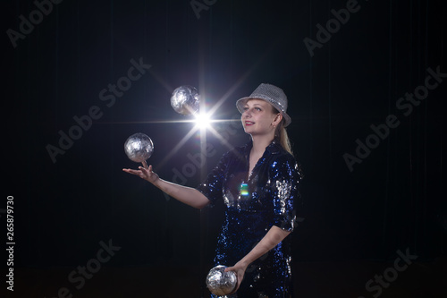 Circus actress performs. The girl juggles balls on a dark background in the spotlights.