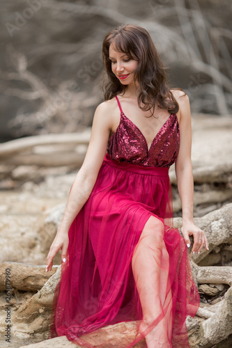 Young beautiful woman is wearing fashion red dress sitting near the waterfall