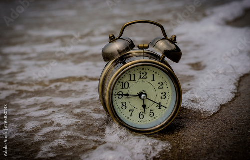 Alarm clock on the beach with waves from the sea and sponges as background. photo