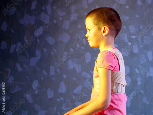 Kid in corrector for spine in pink t-shirt on a gray background .Child wearing back support belt for support and improve back posture photo