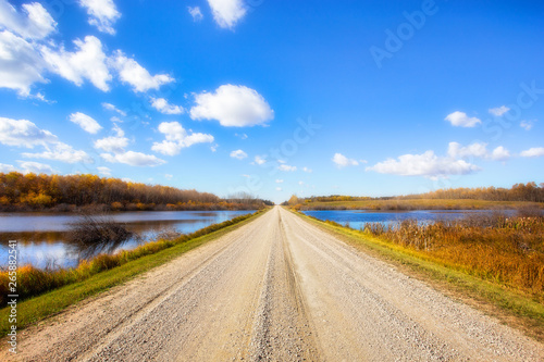 Fotografie A gravel backroad dividing ponds of water sided with autumn colored trees in a p