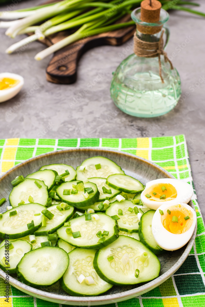 Sliced cucumber with green onions and boiled chicken egg on a plate on the table Sliced cucumber with green onions and boiled chicken egg on a plate on the table