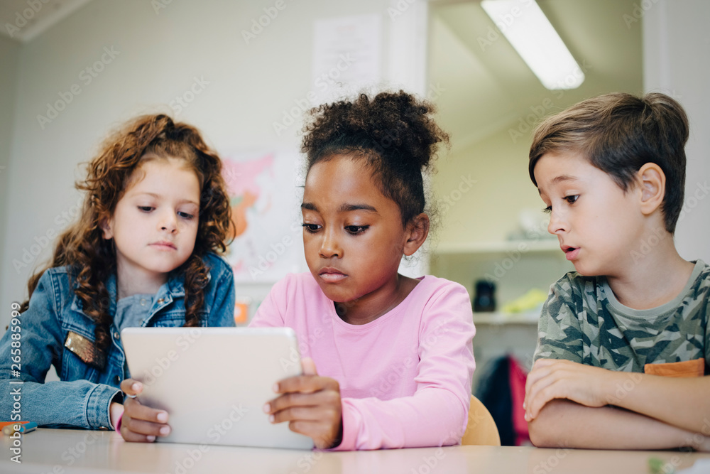 School friends learning through digital tablet at desk in classroom School friends learning through digital tablet at desk in classroom
