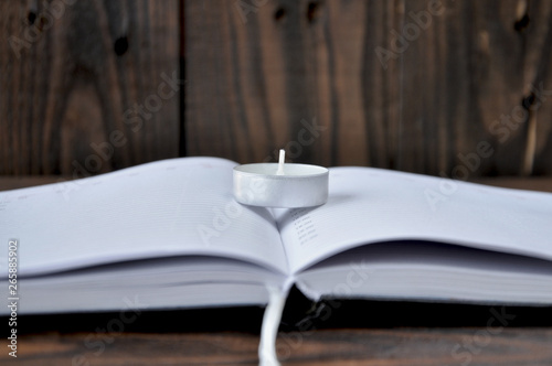 open notepad lying on a wooden table. There is a small candle on the notebook. The background is pinkish.