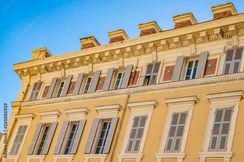 View to the decorated facade of a historic house in Nice, France. You can see the typical windows and shutters of a Mediterranean cityscape.