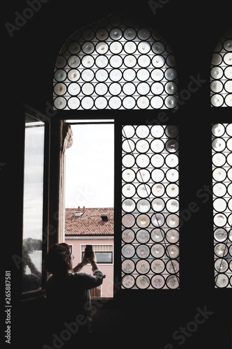 Rear view of woman taking picture through arched window with leaded glass in Venice, Veneto, Italy. photo