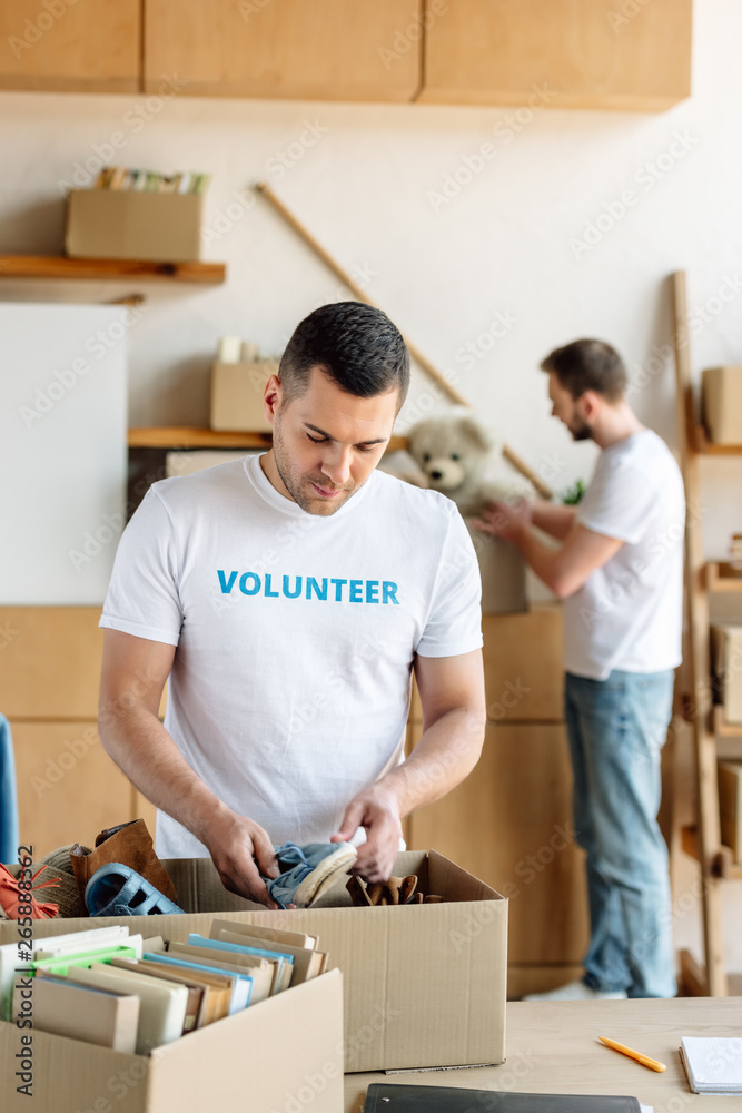 selective focus of handsome volunteer unpacking carton box with footwear selective focus of handsome volunteer unpacking carton box with footwear
