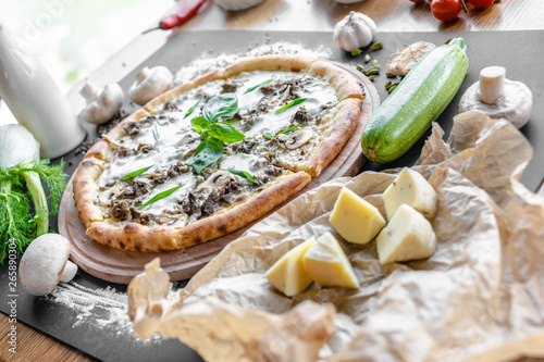 Pizza with zucchini, mushrooms, cheese. Pepper, zucchini, champignons, garlic,  onion and piece of cheese near on the table. Horizontal image. Shallow focus.  Natural light. Black background. 