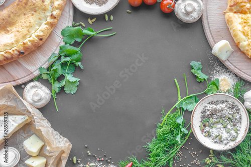 Vegetables, champignons, onions, tomato, dill, parsley, cheese, pies on wooden boards, bowl with spices. Black background, top view, flat lay. Horizontal image. Copy space.
