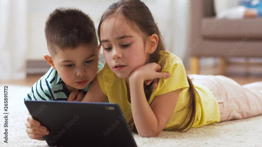 childhood, technology and family concept - little brother and sister with tablet pc computer lying on floor at home childhood, technology and family concept - little brother and sister with tablet pc computer lying on floor at home
