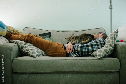 Tabby cat sleeps on the chest of a man asleep on couch