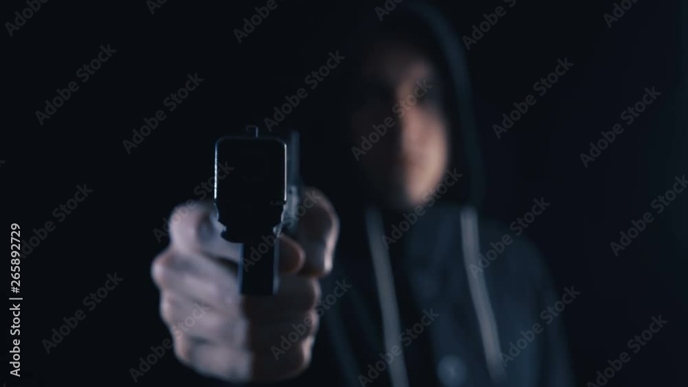 Mercenary or assassin in the hood is aiming with a pistol on a black background. Mercenary or assassin in the hood is aiming with a pistol on a black background.