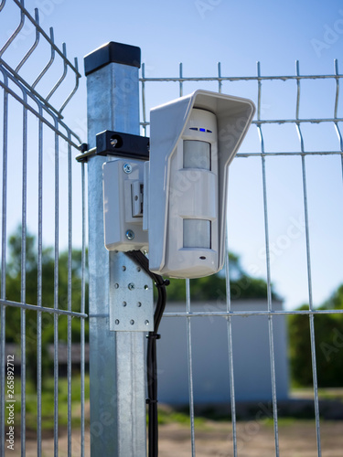 Motion sensor on open protected area. Installed on the fence and connected to the security system with wires. Multifunctional microwave detector. Outdoor guard. Concept of personal or object security.