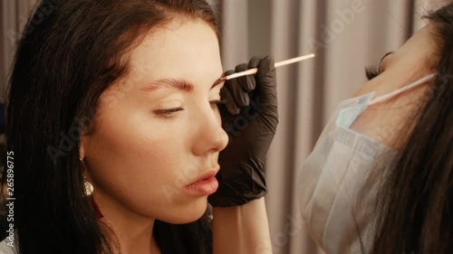 Woman cosmetologist apply paint with brush on the eyebrows of a beautiful patient. Part of eyebrow correction procedure close-up. Professional care for face in beauty saloon photo