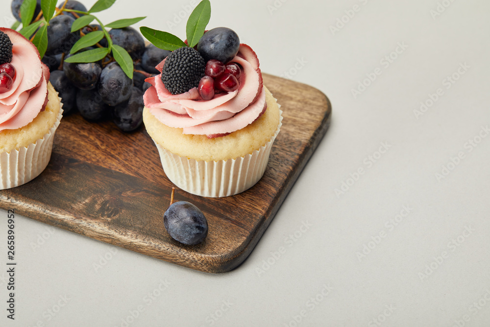 wooden cutting board with sweet cupcakes isolated on grey