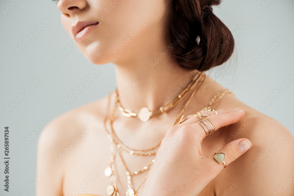 cropped view of young woman with shiny lips in golden necklaces and rings isolated on grey