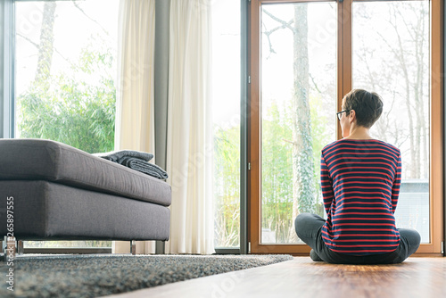 Back view of woman sitting on the floor of living room looking out of window