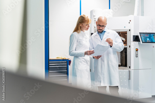 Two technicians wearing lab coats looking at plan photo