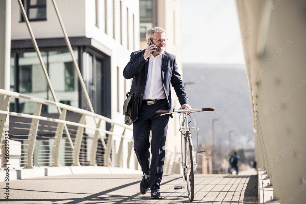 Smiling mature businessman with bicycle talking on cell phone in the city Smiling mature businessman with bicycle talking on cell phone in the city