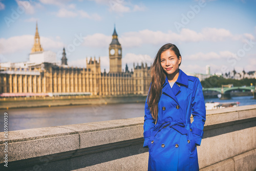 London woman european city traveler in blue trench coat outerwear at famous UK travel destination, Westminster Big Ben on Thames river. Europe holiday Asian businesswoman happy in Autumn vacation. photo