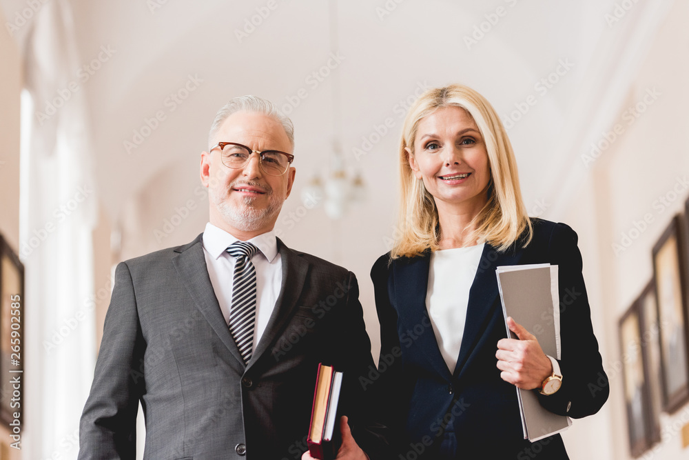 low angle view of cheerful teachers looking at camera while holding books low angle view of cheerful teachers looking at camera while holding books