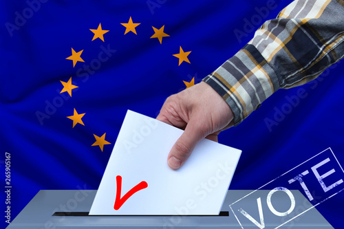 Male hand puts down a white sheet of paper with a mark as a symbol of a ballot paper against the background of the EU flag, symbol of elections to the European Parliament