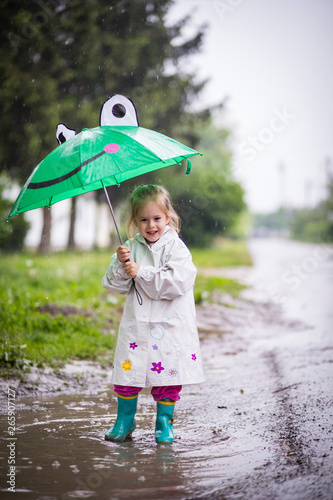 Happy child playing in the rain. Little girl with umbrella having fun outdoor .