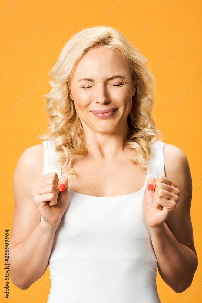 emotional blonde woman standing with closed eyes isolated on orange