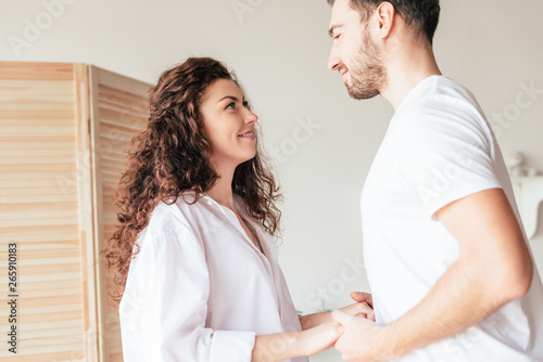 smiling couple holding hands and looking at each other in bedroom