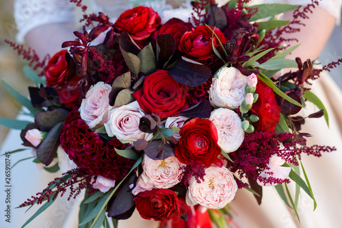 Unsuspected bride holds in her hands an exquisite wedding bouquet of red and pink roses