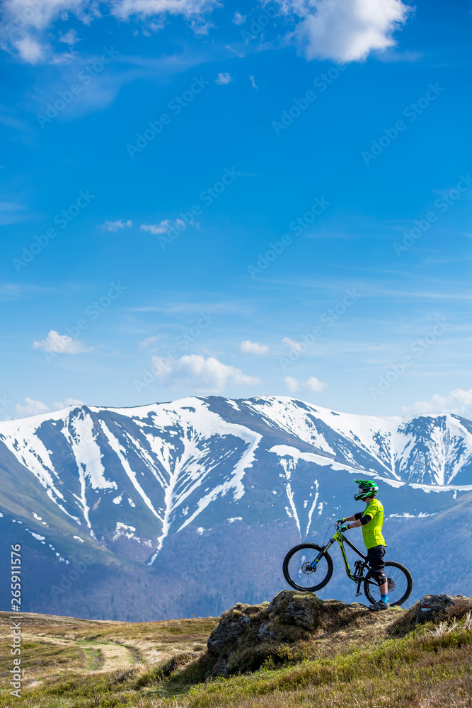 A man stands with a bike on top of the mountain..