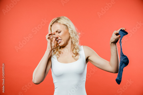 Картината върху платно curly blonde woman touching nose while holding smelly dirty sock on red