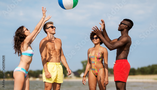 friendship, summer holidays and people concept - happy friends playing with inflatable ball on beach