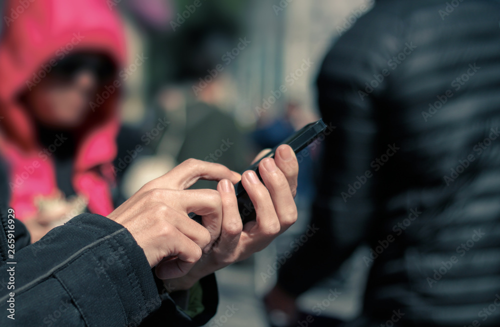 Man holding and typing on mobile phone on the street, crowd of people in background. Technology addiction.