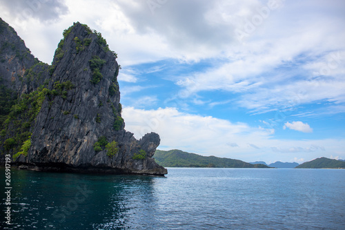 Tropical island in sea. Black cliff and blue sky landscape. Philippines island hopping. Black rock in still seashore.
