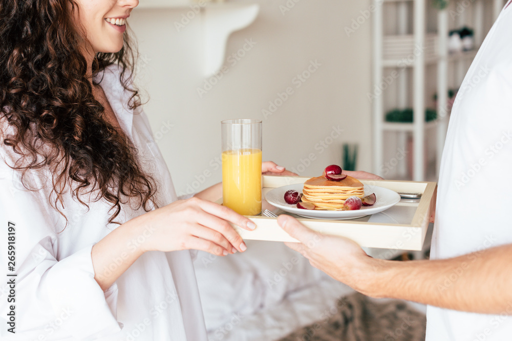partial view of couple holding tray with pancakes and orange juice in bedroom partial view of couple holding tray with pancakes and orange juice in bedroom