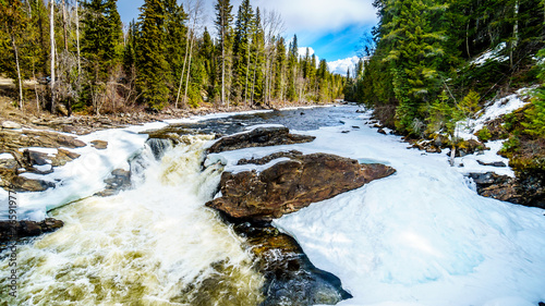 Water of the Murtle River tumbles over the edge of the partly frozen Mushbowl Falls in the Cariboo Mountains of Wells Gray Provincial Park, British Columbia, Canada
