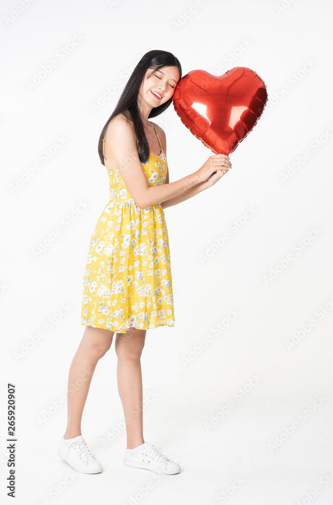 Asian young woman in yellow dress hold red balloon heart. Young woman holding it with being excited and surprised holiday present isolated white background.concept love surprise valentine day. Asian young woman in yellow dress hold red balloon heart. Young woman holding it with being excited and surprised holiday present isolated white background.concept love surprise valentine day.