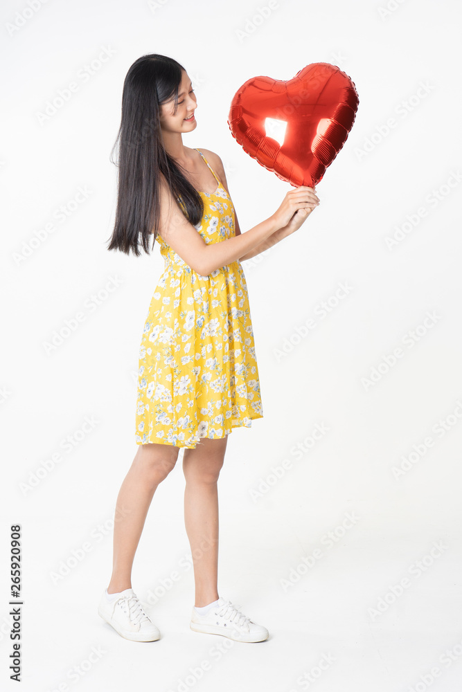Asian young woman in yellow dress hold red balloon heart. Young woman holding it with being excited and surprised holiday present isolated white background.concept love surprise valentine day. Asian young woman in yellow dress hold red balloon heart. Young woman holding it with being excited and surprised holiday present isolated white background.concept love surprise valentine day.