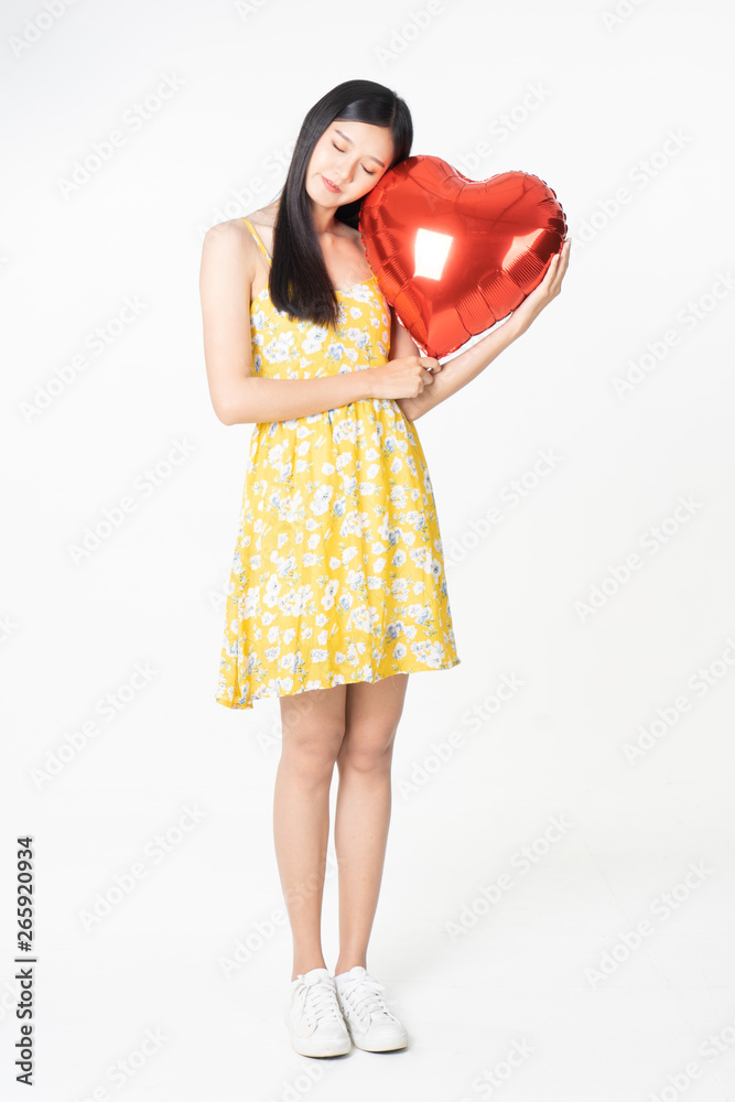 Asian young woman in yellow dress hold red balloon heart. Young woman holding it with being excited and surprised holiday present isolated white background.concept love surprise valentine day. Asian young woman in yellow dress hold red balloon heart. Young woman holding it with being excited and surprised holiday present isolated white background.concept love surprise valentine day.