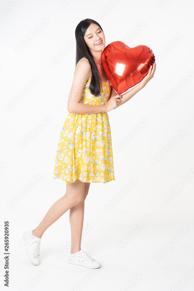 Asian young woman in yellow dress hold  red balloon heart. Young woman holding it with  being excited and surprised  holiday present isolated white  background.concept love surprise valentine day.