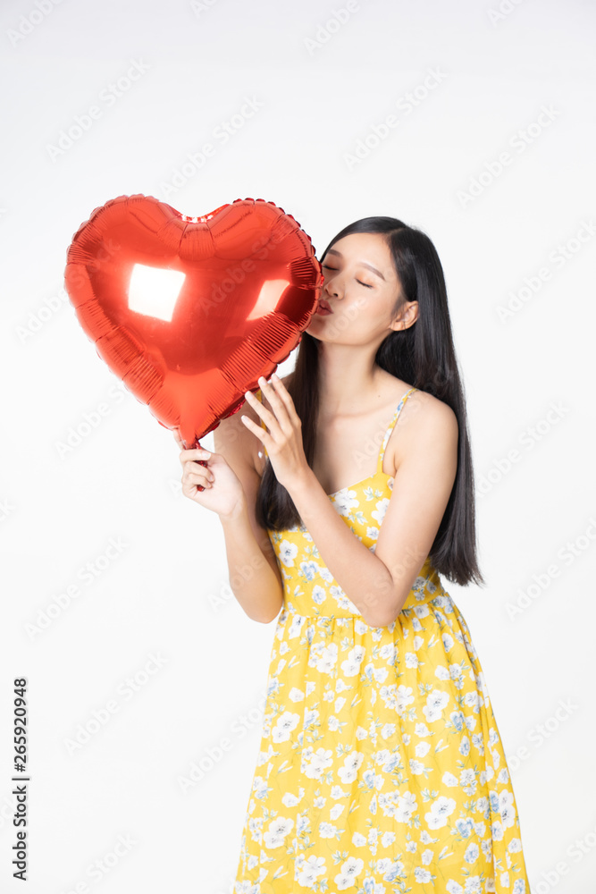 Asian young woman in yellow dress hold  red balloon heart. Young woman holding it with  being excited and surprised  holiday present isolated white  background.concept love surprise valentine day.