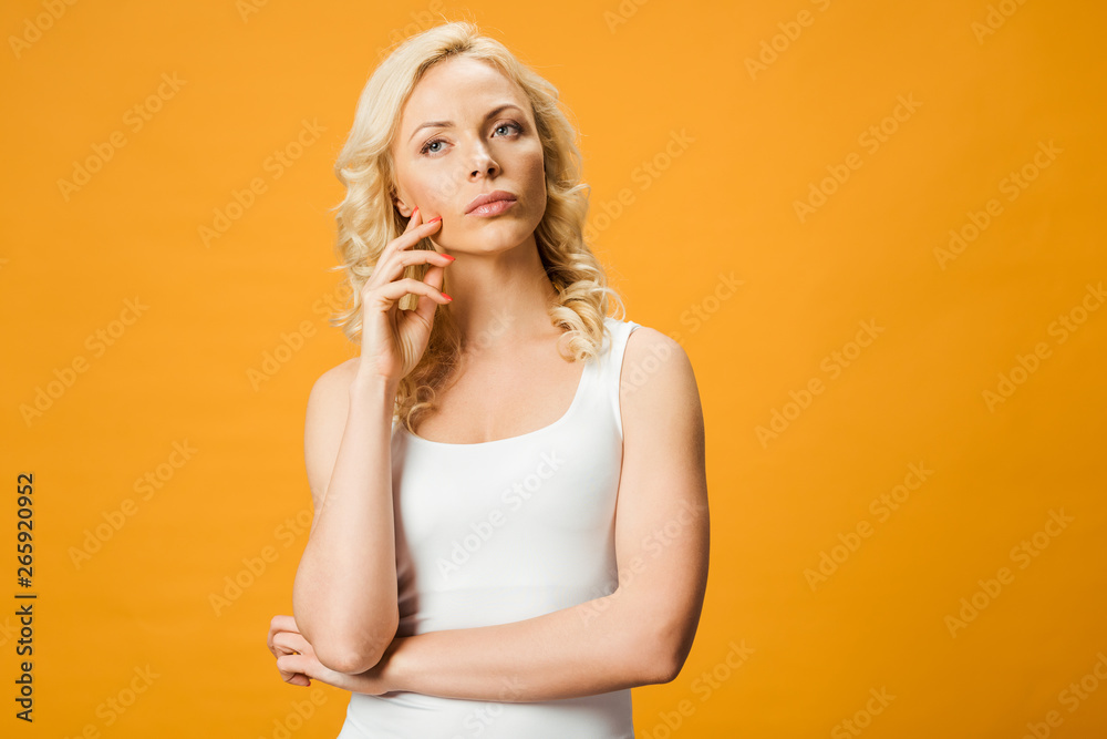 pensive blonde woman thinking while standing isolated on orange pensive blonde woman thinking while standing isolated on orange